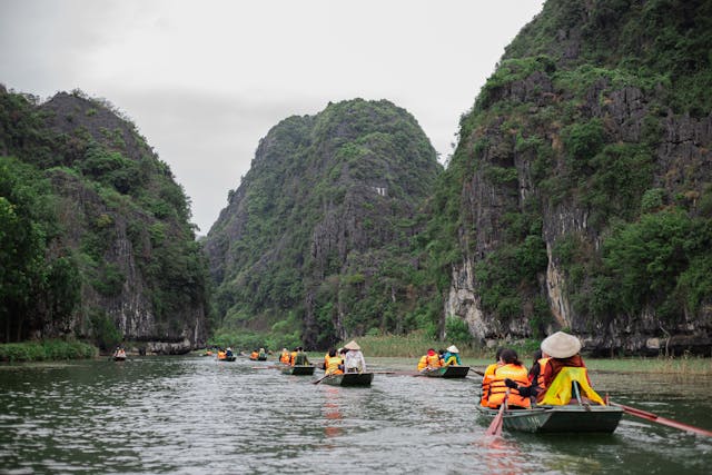 People on small rowboats along the Ngo Dong River in Ninh Binh, surrounded by limestone cliffs and green countryside